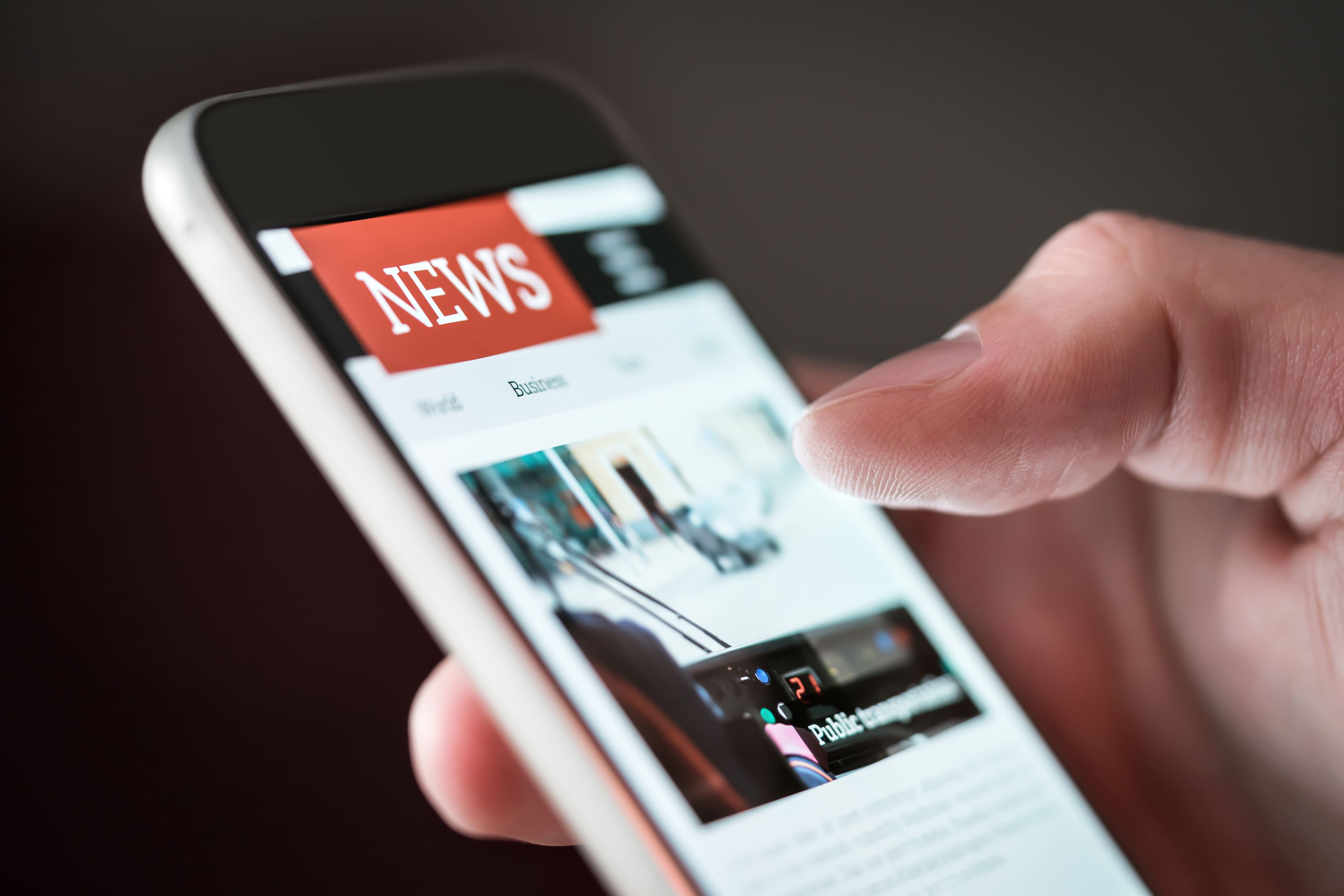 Foto em close de um polegar tocando tela de smartphone com um site de notícias aberto