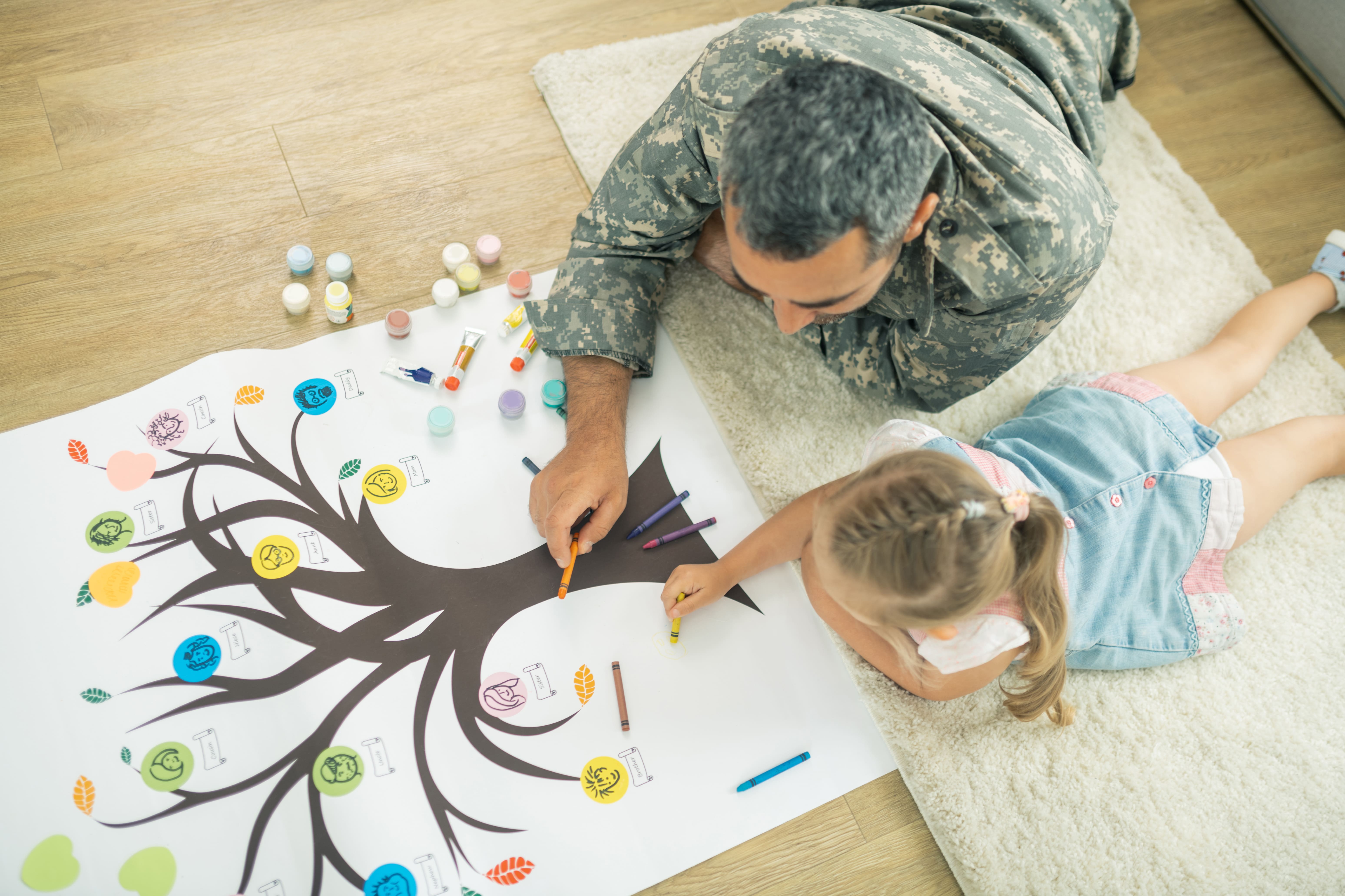 Pai e filha deitados no chão colorindo e produzindo o desenho da árvore genealógica