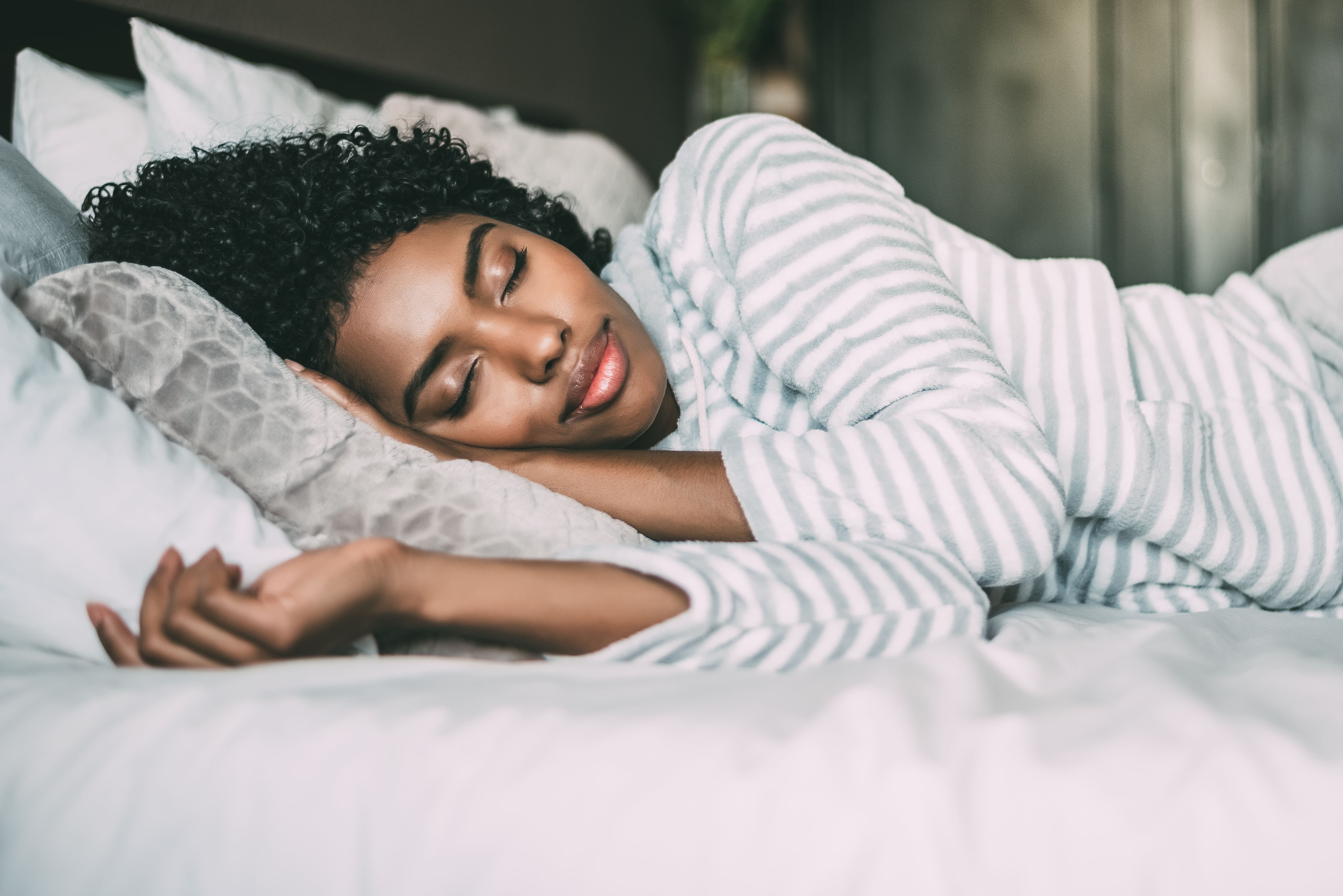close-up de uma linda mulher negra com cabelos cacheados dormindo na cama olhos fechados