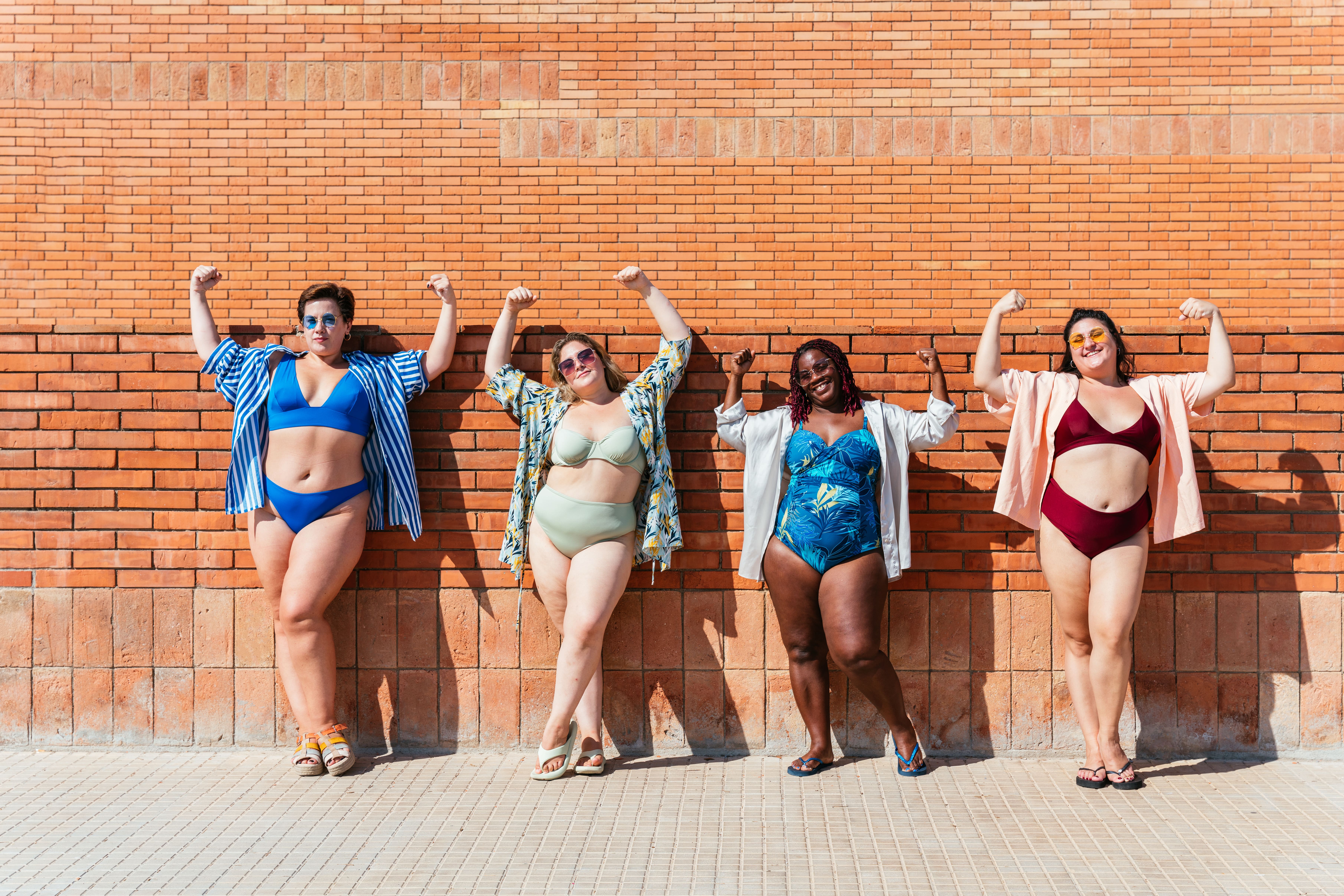 grupo de bonitas mulheres plus size com roupas de praia contraindo os músculos dos braços