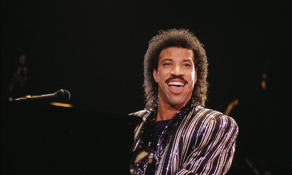 Lionel Richie sorrindo em show sentado no piano