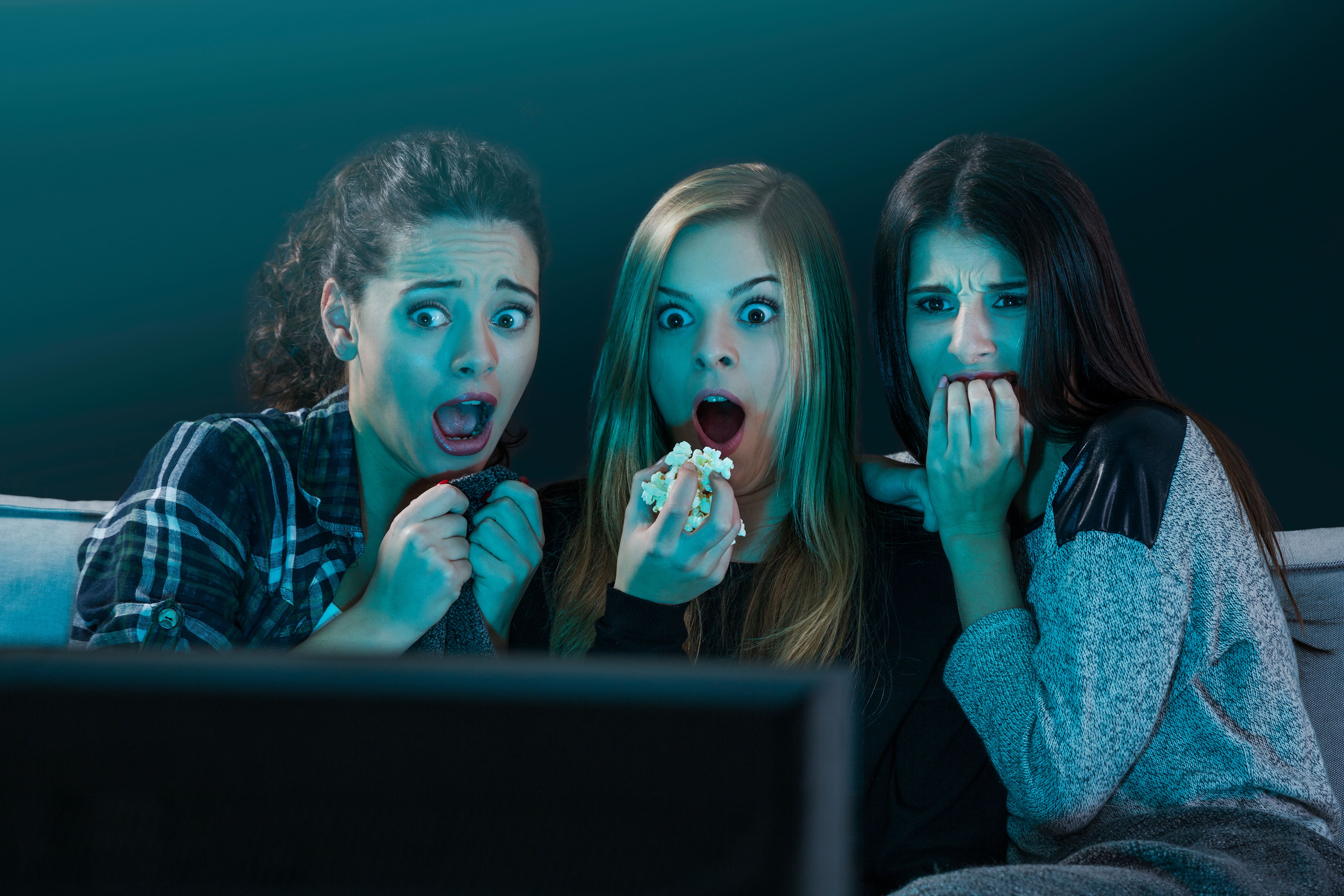 Três mulheres com expressões de medo enquanto assistem algo na televisão.