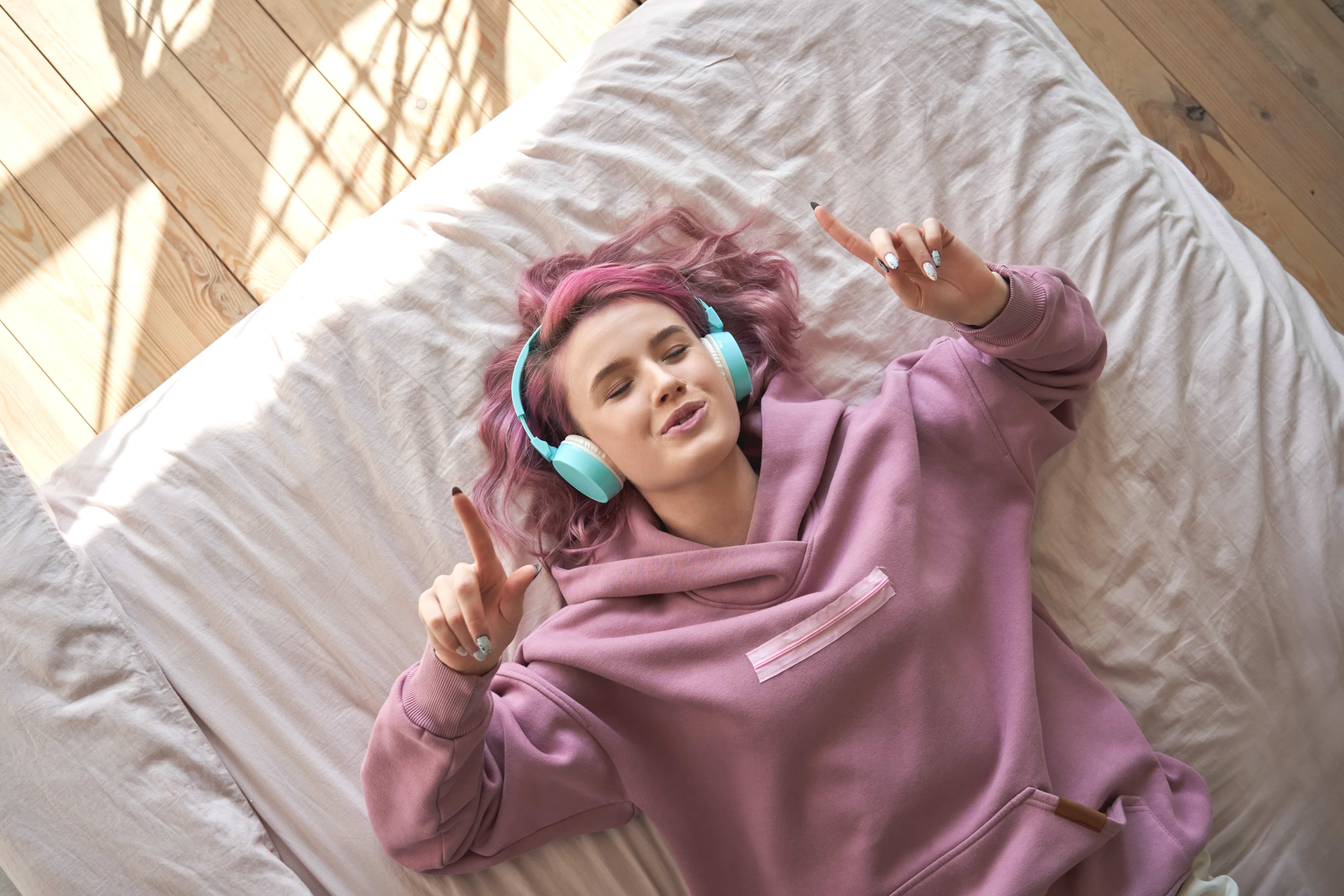 garota com cabelo rosa deitada na cama escutando música nos headphones